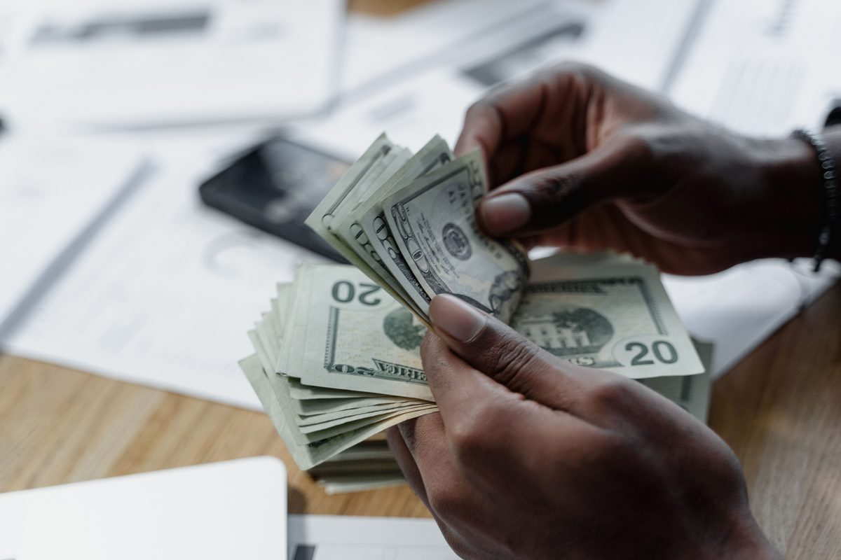Hands counting US dollar bills on a desk with a smartphone — representing Credit Genie Cash Boost